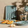 Green baking utensils set with tray, mixing bowl, rolling pin, whisk, and pastries.