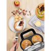 Pie maker with two golden pies, served with ice cream and fruit, on a kitchen worktop