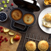 Pie maker with two golden pies, surrounded by fruit and ingredients on kitchen counter