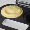 Uncooked round pie in a silver pie maker appliance, shown on kitchen worktop
