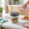 Manual food chopper with grey lid, vegetables inside, shown in use on kitchen counter