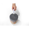 Hand using grey manual food chopper with clear bowl, filled with chopped vegetables
