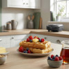 Plate of waffles topped with berries, butter, and syrup in a modern kitchen.
