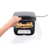 Black sandwich maker with hand placing toasted sandwich inside, shown from above.