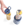 Single-serve blender in navy with fruit-filled cup and hand holding smoothie bottle lid
