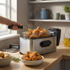 Stainless steel deep fat fryer with basket of cooked fried chicken on kitchen counter