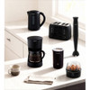 Black electric kettle pouring hot water into patterned mug on kitchen table
