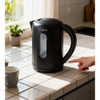 Black electric kettle on tiled kitchen counter, hand pressing power switch