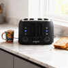 Black 4-slice toaster on kitchen counter with kettle, mug, and slice of bread nearby