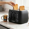 Hand placing slice of bread into 4-slot black toaster with other bread slices inside