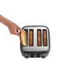 Hand placing slice of bread into 4-slot black toaster with other bread slices inside