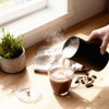 Milk frother pouring steamed milk into hot chocolate in glass mug on kitchen worktop