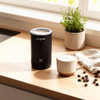 Black electric milk frother on kitchen counter with cup of frothed coffee