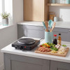 Black single electric hot plate on kitchen worktop beside utensils and ingredients for stir fry