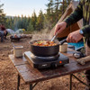Progress single electric hot plate cooking pasta at campsite, tent and campfire in background