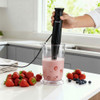 Black hand blender mixing strawberry smoothie in jug, fresh berries on countertop