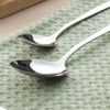 Two stainless steel serving spoons on a light green textured cloth