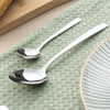 Two stainless steel spoons on green textured cloth, shown next to a plate