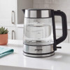 Glass and stainless steel electric kettle pouring hot water into a blue mug