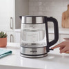 Glass and stainless steel electric kettle with water level marks, switched on in kitchen.