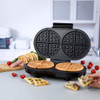 Black waffle maker with two golden waffles inside, hand opening the lid.