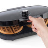 Black waffle maker with two golden waffles inside, hand opening the lid.