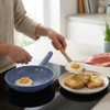 Blue non-stick frying pan cooking fried eggs, transferring egg onto buttered toast