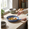 Blue non-stick frying pan with colourful vegetables being stirred on a kitchen worktop