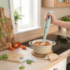 Light green hand blender blending tomato soup in cream pot on kitchen counter