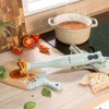 Light green hand blender blending tomato soup in cream pot on kitchen counter