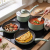 Set of two green saucepans with glass lids, steaming on a hob in a kitchen setting