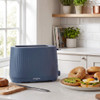 Blue 2-slice toaster on kitchen counter with bagels, avocado and eggs nearby