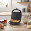Waffle maker with two cooked waffles on kitchen counter, surrounded by baking ingredients.