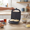 Open waffle maker on kitchen counter, shown with batter and toppings ready for use