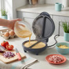 Omelette maker in use with chopped onions, cheese, eggs and seasoning visible nearby