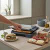 Electric sandwich press toasting panini on kitchen counter with fresh ingredients nearby