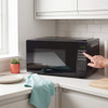 Woman in apron stirring chocolate batter by microwave in modern kitchen
