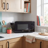 Black microwave oven on kitchen counter, hand turning dial, with oats and fruit nearby