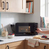 Black microwave oven on kitchen counter, hand turning dial, with oats and fruit nearby