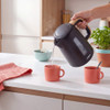 Black electric kettle with wood-effect handle, shown in use on a kitchen counter