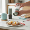 Green salt and pepper grinder set in use, seasoning poached eggs on toast at breakfast table