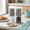 Set of two clear glass spice jars with sage green lids, suitable for kitchen storage.
