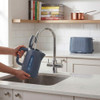 Blue electric kettle being filled at kitchen sink, matching blue toaster on counter