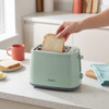Green two-slice toaster with bread being inserted, shown on a kitchen counter
