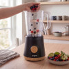Black blender on kitchen counter with hand adding mixed berries to jug