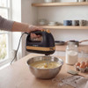 Black and wood effect hand mixer mixing cake batter in a metal bowl on kitchen counter