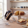 Black hand mixer with wooden accents next to a lemon cake on stand, cake slices in foreground