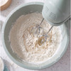 Electric hand mixer blending flour and liquid in a pale green mixing bowl