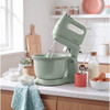 Green stand mixer with bowl on kitchen counter, surrounded by fresh baked goods