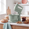 Green stand mixer with bowl on kitchen counter, surrounded by fresh baked goods